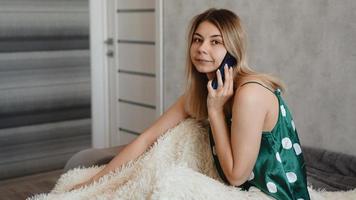 attraktiv ung kvinna som sitter i sängen och pratar på smartphone