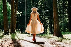 en ung kvinna i en vit klänning och en halmhatt går genom skogen foto