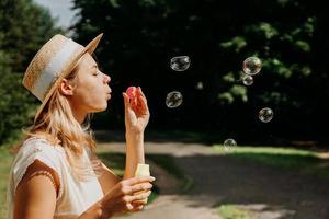 söt blond kvinna som blåser såpbubblor. vacker grön park foto
