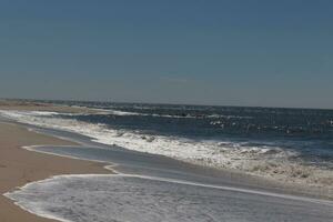 detta skön strand bild var tagen på cape Maj ny jersey. den visar de vågor porlande in i de Strand och de Söt brun sand. de blå himmel med de liten bit av moln rapportering lägger till till detta. foto