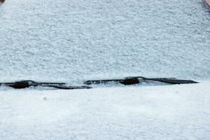 snö täckt bil vindskydd, vindrutetorkare och hätta foto