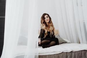 vacker sexig brun lockigt långt hår kvinna poserar i sängen