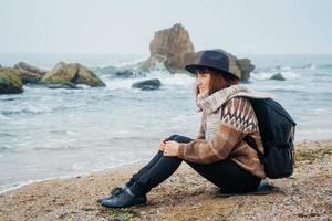 kvinna i en hatt med en ryggsäck på bakgrund av hav och stenar foto