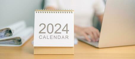 2024 år kalender på tabell med företag kvinna använder sig av bärbar dator dator. nedräkning, Lycklig ny år, upplösning, mål, planen, handling, uppdrag och finansiell begrepp foto