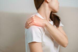 kvinna har axel och nacke smärta under Sammanträde på soffa på Hem. muskel smärtsam på grund av till myofascial smärta syndrom och fibromyalgi, reumatism, scapular smärta, cervical ryggrad. ergonomisk begrepp foto