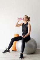 passande kvinna dricker vatten efter att ha tränat sittande på fitball foto