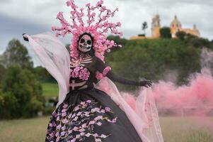 förtjusande catrina en dia de los muertos fotografering i cholulas cempasuchil fält, inramade förbi de ikoniska kolula kyrka fira skönhet tradition och de förtjusande rosa rök foto