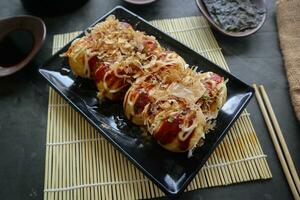 takoyaki är en japansk mat, tillverkad från vete mjöl deg, bläckfisk kött, eller Övrig fyllningar, eras med sås, majonnäs och garnering i de form av katsuobushi eller trä fisk spån. foto