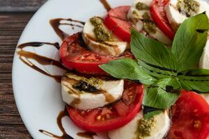 tallrik av friska klassisk utsökt caprese sallad med tomater och mozzarella ost med färsk basilika löv på ljus Linné bordsduk stänga upp. italiensk kök begrepp foto