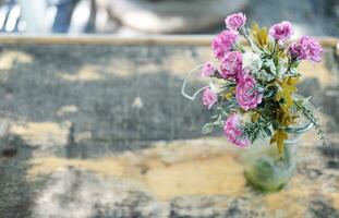 liten blomma rosa blommor i glas vas dekorerad på årgång trä- tabell i naturlig trädgård hus foto