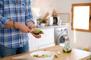 närbild manlig kock skärande avokado frukt, framställning en färsk rå vegan sallad från organisk grönsaker, i de Hem kök foto