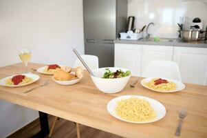 en eras tabell med traditionell italiensk spaghetti och tomat sås i vit tallrikar, en skål med hälsosam sallad och vin foto