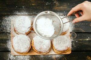 matlagning traditionell hanukkah sufganiyot. kvinna strössel munkar med pulveriserad socker. foto