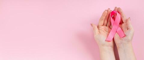 bröst cancer medvetenhet månad. kvinnas hand innehar rosa band. hälsa vård begrepp, cancer kontrollera symbol. foto