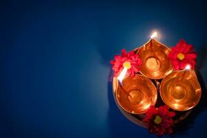 Lycklig diwali. fira de indisk festival av ljus. traditionell diya olja lampor och röd blommor på blå bakgrund foto