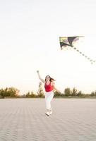ung kvinna som flyger en drake i en offentlig park vid solnedgången foto