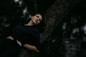 kvinna i svarta kläder på en bakgrund av vatten, ligger på ett träd foto
