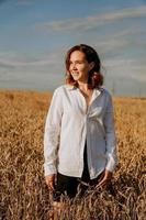 glad ung kvinna i en vit skjorta i ett vetefält. solig dag. foto