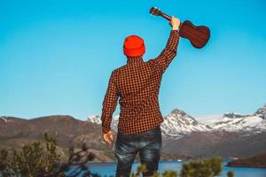 kille med en gitarr på bakgrunden av berg, skogar och sjö