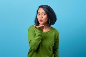 attraktiv asiatisk kvinna skicka air kiss på blå bakgrund foto