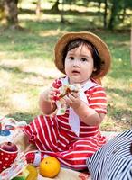 söt liten bebis i en röd klänning och srtaw hatt på en picknick i parken foto