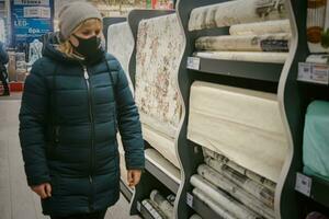 kiev ukraina - 03 03 2021 kvinna i vinter- kläder och mask i en Lagra väljer diy Lagra köpcenter. tapet i de Lagra av efterbehandling material. handel hall med flerfärgad tapet på de väggar. foto