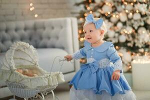 bebis flicka bär söt klänning och pannband, bär sittvagn i festligt dekorerad rum med krans av lampor. foto