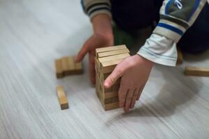 en barn klädd inte ordentligt i en Hem kläder spelar på de golv. man bygger en torn av trä- barer. foto