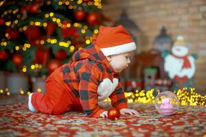 liten överraskad barn i santa kostym i festlig rum på jul eve. flicka på bakgrund av jul träd. foto