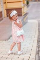 skön flicka i en rosa klänning med väska på axlar vände sig och tittade Bakom honom. hild försöker en ny klänning. foto