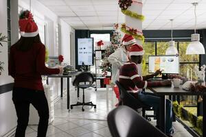 multietniskt företag team arbetssätt med grafer i festlig dekorerad kontor under jul säsong. hård arbetssätt anställda kontroll bokföring diagram runt om xmas Semester foto