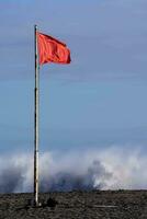 en röd flagga på de strand med vågor kraschar i de bakgrund foto