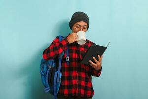 ung asiatisk manlig studerande tar en kaffe ha sönder efter föredrag, isolerat på blå bakgrund foto