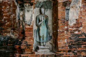 en buddha staty är i de mitten av ett gammal tegel vägg foto