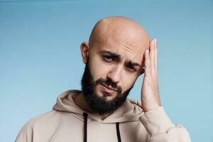 arab man lidande från huvudvärk, innehav hand på huvud i smärta porträtt. ung vuxen skallig skäggig man har migrän medan ser på kamera med utmattad ansiktsbehandling uttryck foto