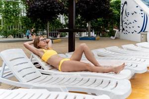 den vackra unga kvinnan som ligger på solstolen bredvid poolen foto