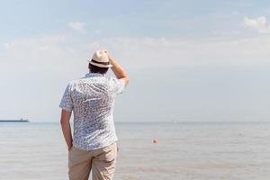ung man i sommarkläder som står på en pir, havet i bakgrunden foto