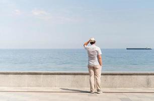 ung man i sommarkläder som står på en pir, havet i bakgrunden foto