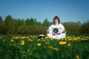 kvinna astronaut utan hjälm sitter på en grön gräsmatta bland blommor foto