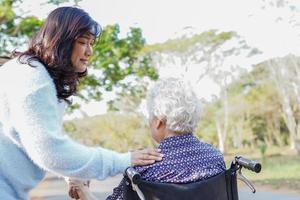 hjälp och vård asiatisk senior kvinna sitter på rullstol i parken. foto