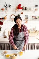 ung latinsk kvinna som vispar ägg som lagar mat i köket foto