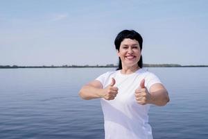 kvinna i sportkläder visar tummen upp träna nära floden foto