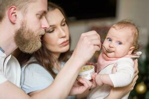 far och mor utfodra deras bebis frukt puré i de kök från en sked foto