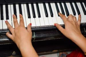 asiatisk pojke spelar de synthesizer eller piano. söt liten unge inlärning på vilket sätt till spela piano. barnets händer på de tangentbord inomhus. foto