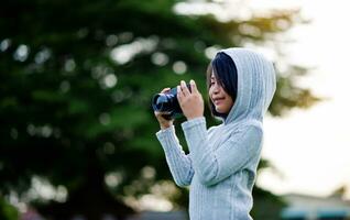 ta bilder med en mirror kamera. liten flicka praktiserande natur fotografi liten fotograf de glädje av tar bilder foto