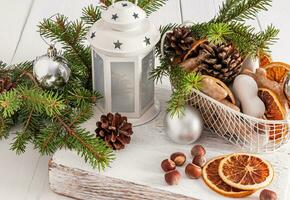 jul lykta, korg med glaserad pepparkaka och torkades orange skivor, grön gran grenar på vit trä- tabell. en traditionell behandla. bokeh. foto