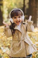 glad liten flicka som lyssnar på musik på hörlurar i höstparken. foto