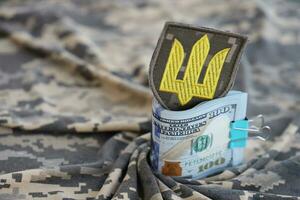 ukrainska armén symbol och knippa av dollar räkningar på militär enhetlig. betalningar till soldater av de ukrainska armén från förenad stater, löner till de militär. krig Stöd foto