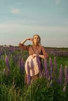 en skön kvinna i en sugrör hatt promenader i en fält med lila blommor. en promenad i natur i de lupin fält foto
