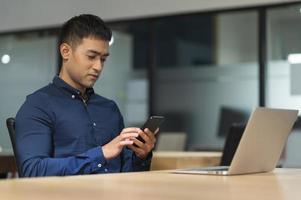 ung asiatisk affärsman som använder smartphone medan han arbetar på kontoret. foto